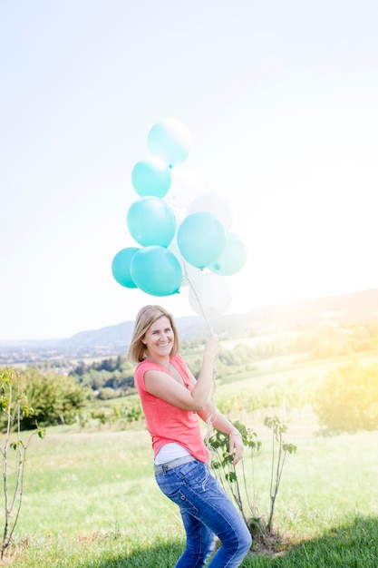 Foto comprimento completo de jovem sorridente segurando balões contra o céu claro
