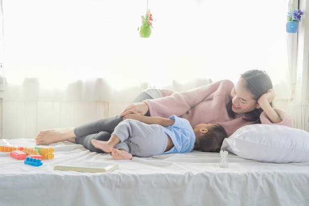 Foto comprimento completo de mãe deitada na cama com o filho em casa