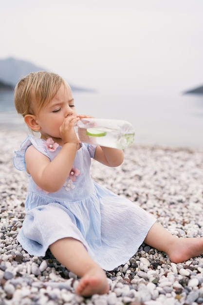 Comprimento completo de menina bebendo limonada sentada na praia