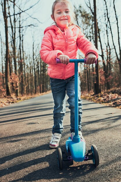 Foto comprimento completo de menina bonita de pé em scooter na floresta