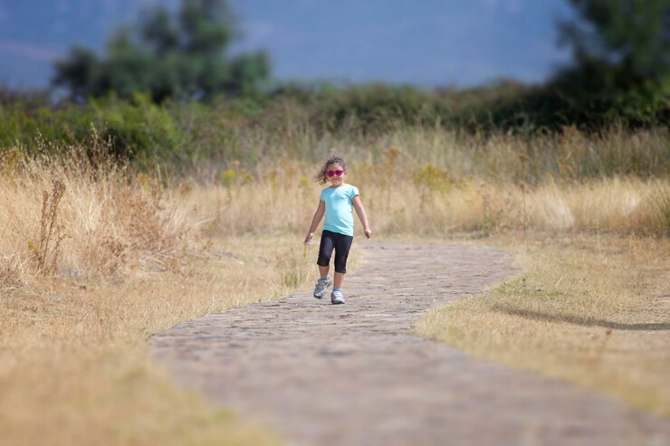 Foto comprimento completo de menina caminhando na estrada em meio a um campo gramado contra o céu