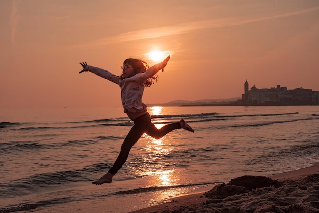 Comprimento completo de menina pulando na praia durante o pôr do sol