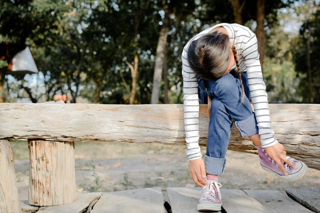 Foto comprimento completo de menina se curvando enquanto está sentada em um tronco de madeira