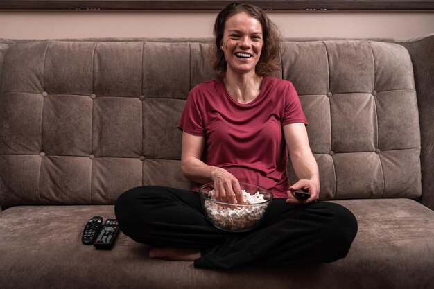 Foto comprimento completo de mulher comendo pipoca sentada no sofá em casa