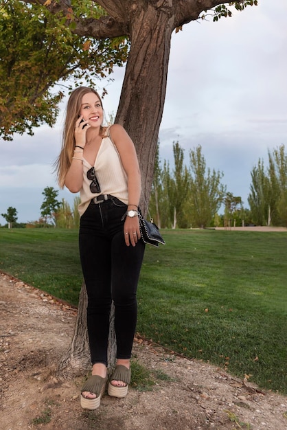 Foto comprimento completo de mulher linda falando ao telefone enquanto está de pé no parque