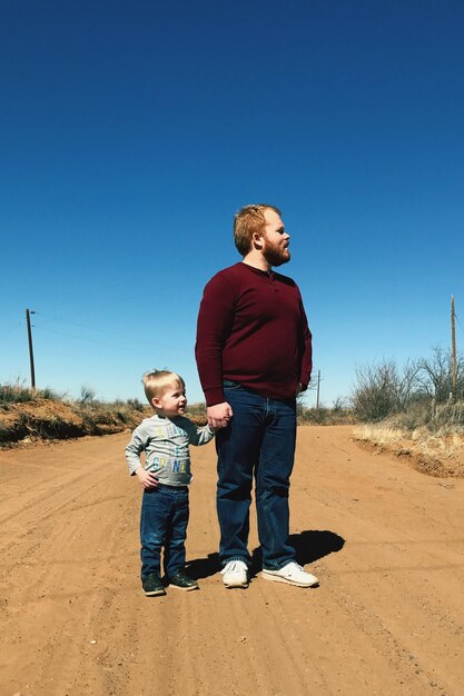 Foto comprimento completo de pai com filho de pé no campo contra o céu azul claro