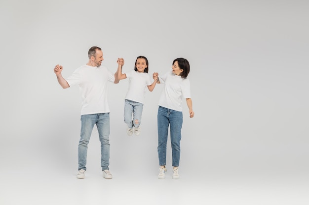 comprimento completo de pais felizes em camisas brancas e jeans de denim azul de mãos dadas e levantando