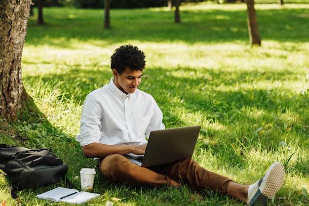 Comprimento completo de um jovem usando um laptop enquanto está sentado no parque