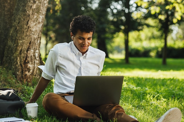 Comprimento completo de um jovem usando um laptop enquanto está sentado no parque