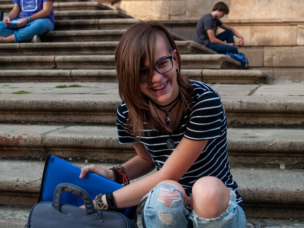 Comprimento completo de uma jovem mulher segurando um arquivo enquanto estava sentada em degraus contra o edifício