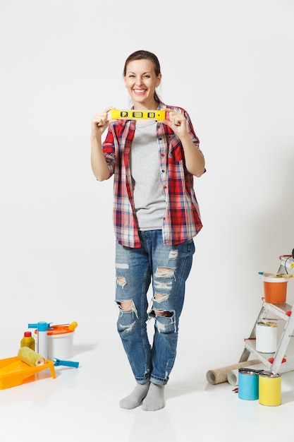 Comprimento total da mulher com construção de pé de nível de bolha de ar perto de instrumentos para casa de apartamento de renovação isolado no fundo branco. Papel de parede, acessórios para colar, ferramentas. Conceito de reparo.