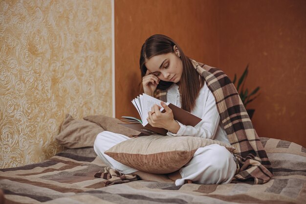 Comprimento total da mulher serena lendo livro e relaxando em xadrez quente na cama em um quarto aconchegante em casa