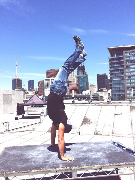 Comprimento total de homem fazendo handstand no terraço da construção em um dia ensolarado