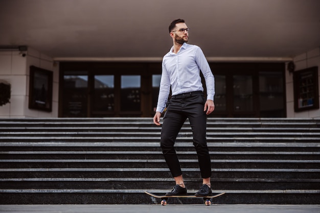 Comprimento total de um atraente homem com barba por fazer elegantemente vestido de skate.