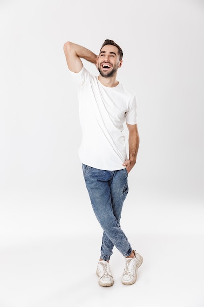 Comprimento total de um homem bonito e alegre, vestindo uma camiseta em branco, isolado na parede branca, posando