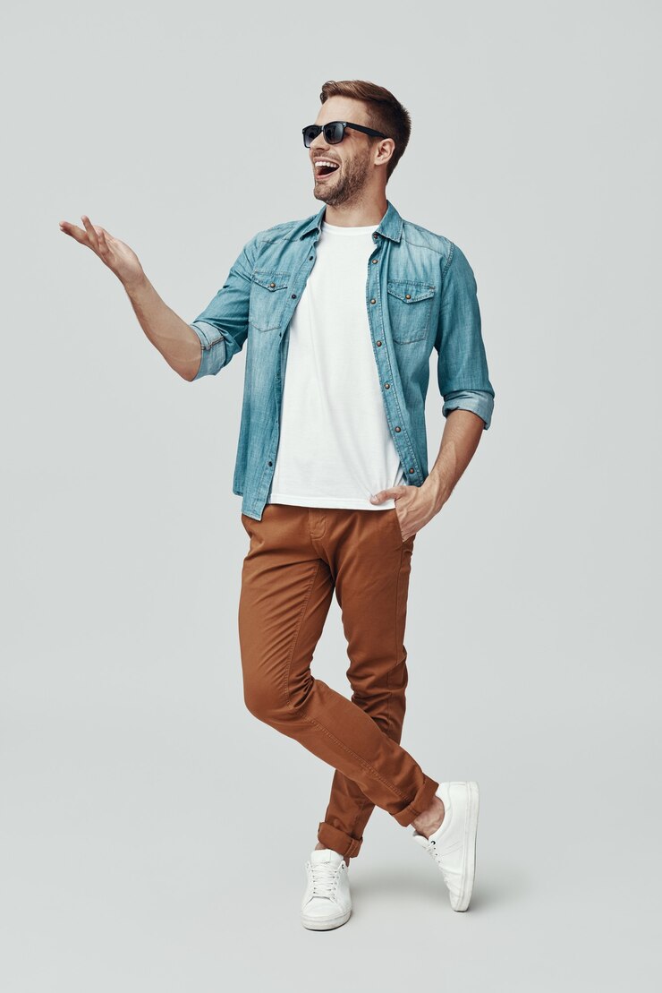Foto comprimento total de um jovem bonito apontando para o espaço da cópia e sorrindo em pé contra um fundo cinza