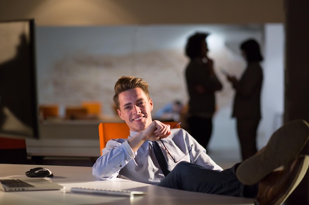 Comprimento total de um jovem empresário casual relaxado sentado com as pernas na mesa no escritório noturno