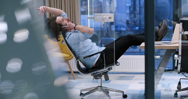 Foto comprimento total de um jovem empresário casual relaxado sentado com as pernas na mesa no escritório