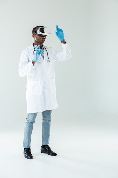 Comprimento total de um médico afro-americano profissional usando óculos de realidade virtual enquanto está envolvido no trabalho