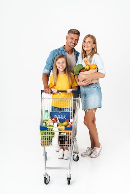 Foto comprimento total de uma família alegre, vestindo roupas casuais, em pé, isolado no branco, comprando mantimentos juntos, carregando sacolas e carrinhos