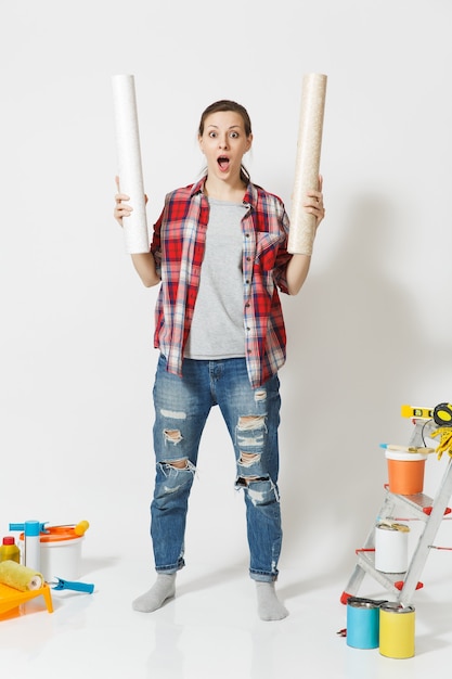 Comprimento total de uma linda mulher com roupas casuais em pé perto de instrumentos para casa de apartamento de renovação isolado no fundo branco. Papel de parede, acessórios para colar, ferramentas de pintura. Conceito de reparo.