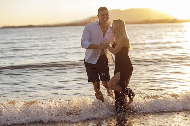 Comprimento total do lindo casal se divertindo enquanto caminhava descalço ao longo da praia