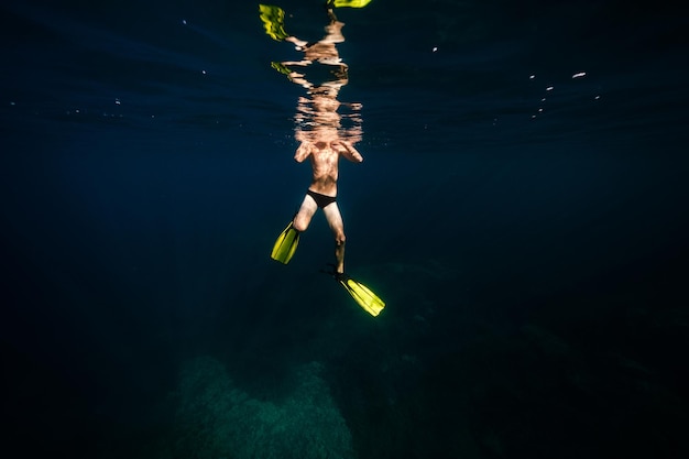 Comprimento total do nadador masculino irreconhecível com torso nu em nadadeiras mergulhando sob a água azul do mar à luz do dia