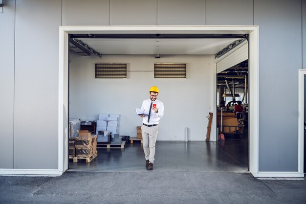 Foto comprimento total do supervisor caucasiano bonito de camisa e gravata e com capacete na cabeça