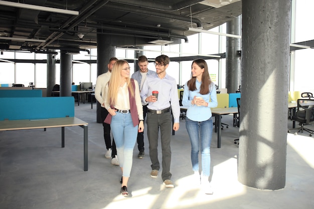 Comprimento total dos jovens em roupas casuais inteligentes, discutindo negócios e sorrindo enquanto caminhava pelo escritório.