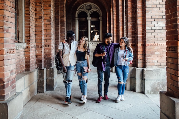 Comprimento total, grupo de estudantes universitários bem-sucedidos e alegres, caminhando pelo campus.