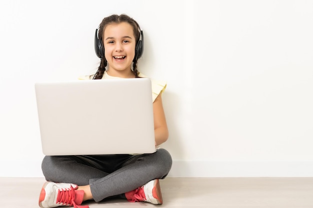 Comprimento total menina sentada no chão, tela de computador portátil, isolada sobre o branco.