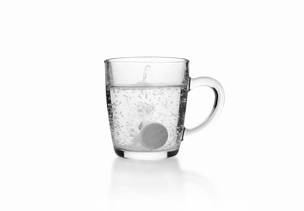 Comprimido efervescente solúvel no fundo de uma caneca de vidro transparente na superfície branca.