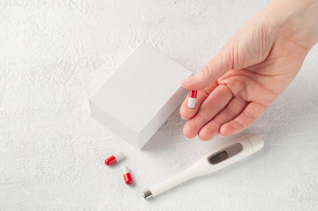 Foto comprimido em uma mão feminina na mesa está uma maquete de uma caixa branca vazia para embalagem de produtos com medicamentos ou vitaminas local para logotipo e texto