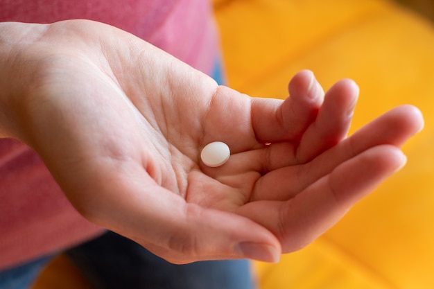 Comprimido ou cápsulas em uma mão feminina em um fundo laranja. Medicamento farmacêutico, remédio em recipientes para saúde, tratamento de pandemia