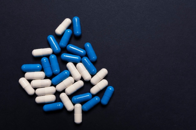 Comprimidos cápsula brancos e azuis em um fundo preto