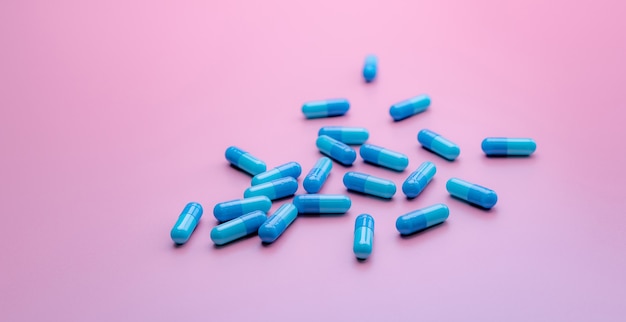 Foto comprimidos cápsula de antibiótico azul espalhados no fundo rosa. resistência a antibióticos. indústria farmacêutica. conceito de cuidados de saúde e medicina. conceito de orçamento de saúde. indústria de fabricação de cápsulas.