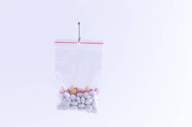 Comprimidos coloridos ou comprimidos pendurados em um pequeno saco ziplock em um anzol de pesca