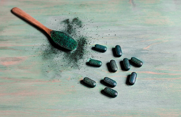 Comprimidos de cevada chlorella spirulina e pó em uma colher de pau sobre um fundo azul de madeira