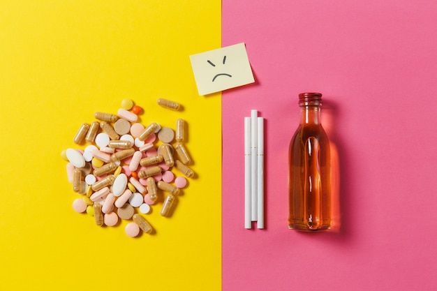 Comprimidos de comprimidos coloridos comprimidos dispostos abstratos, álcool de garrafa, cigarros em fundo de cor rosa rosa amarela