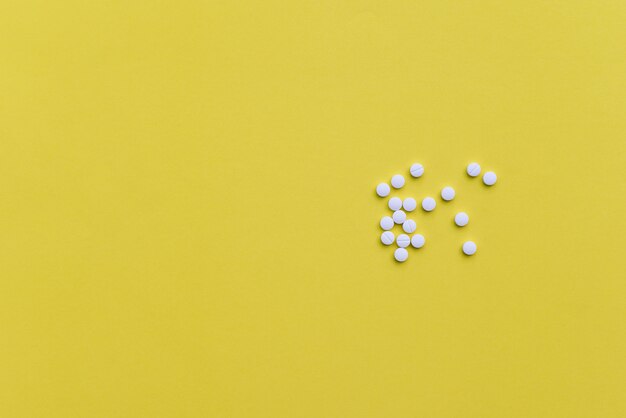 Comprimidos de medicamento branco sobre fundo amarelo