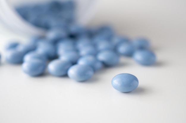 Comprimidos de remédio azul com garrafa no fundo branco