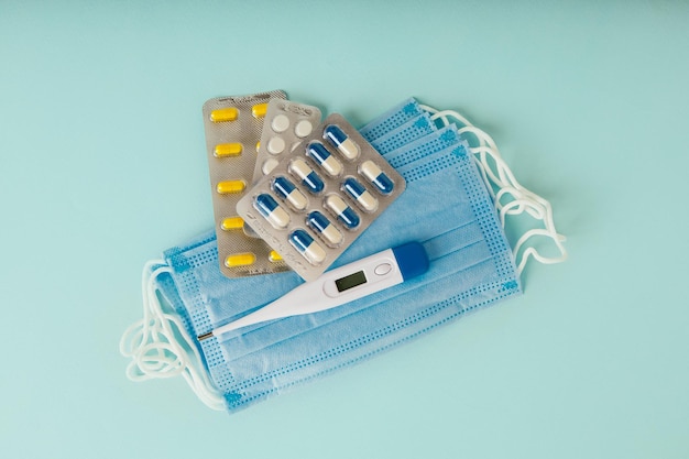 Comprimidos de termômetro e máscara médica em fundo azul Conceito de tratamento