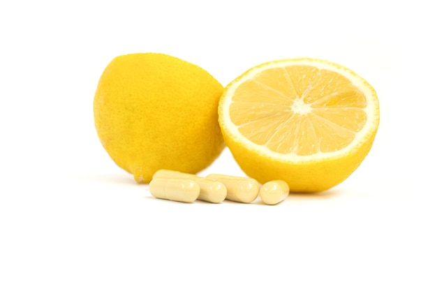 Comprimidos de vitamina C em cápsulas de vitamina C e limão amarelo em fundo branco