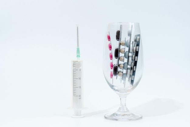 Comprimidos e cápsulas médicas em vidro com seringa isolada no fundo branco