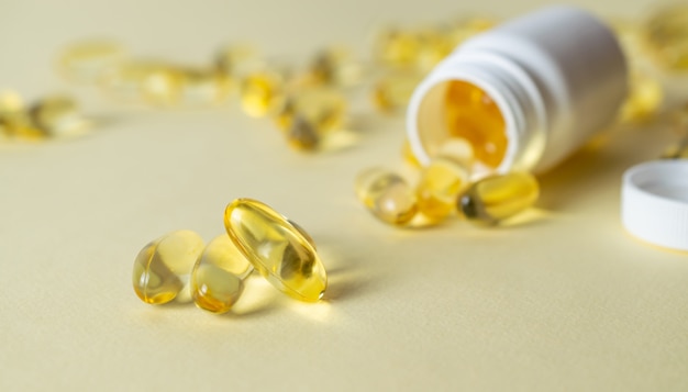 Comprimidos macios dos geles com o óleo Omega-3 que derrama fora do close-up da garrafa de comprimido em um fundo amarelo. Prescrição médica