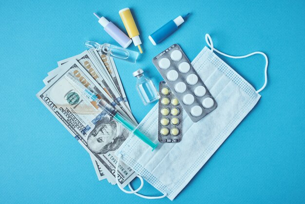 Comprimidos, máscara protetora, itens médicos e notas de dólar em azul
