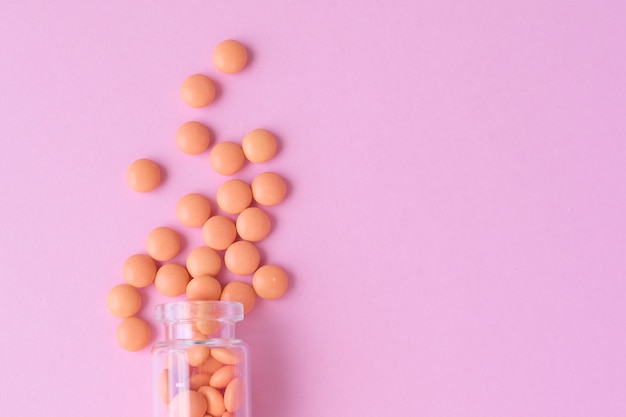 Comprimidos de naranja de botella de vidrio en plano rosado ponen vista superior