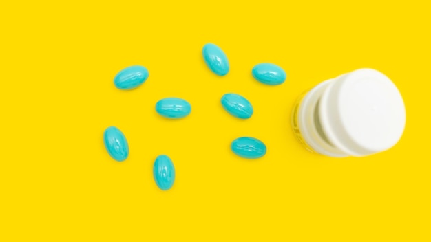 Comprimidos ou cápsulas azuis para tratamento com garrafa branca na vista superior do conceito de farmácia e medicina de fundo amarelo