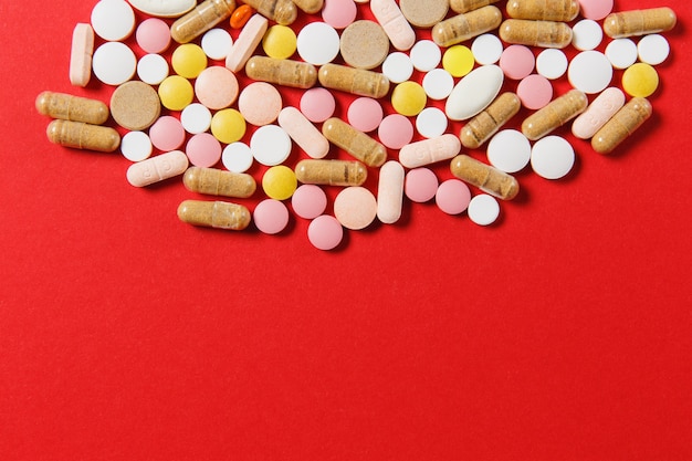 Comprimidos redondos coloridos brancos de medicação dispostos abstratos em um fundo de cor vermelha