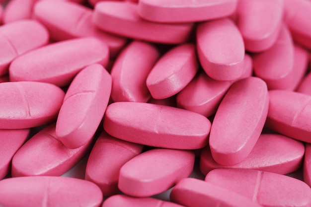 Comprimidos rosa com multivitaminas em tela inteira como pano de fundo.